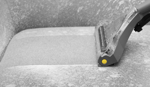 Professional cleaner deep-cleaning a fabric sofa with a hot water extraction tool.