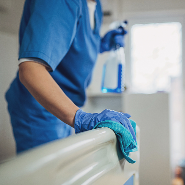 Professional cleaner wiping down treatment tables, sinks, and medical equipment surfaces—maintaining sterile standards in healthcare facilities.